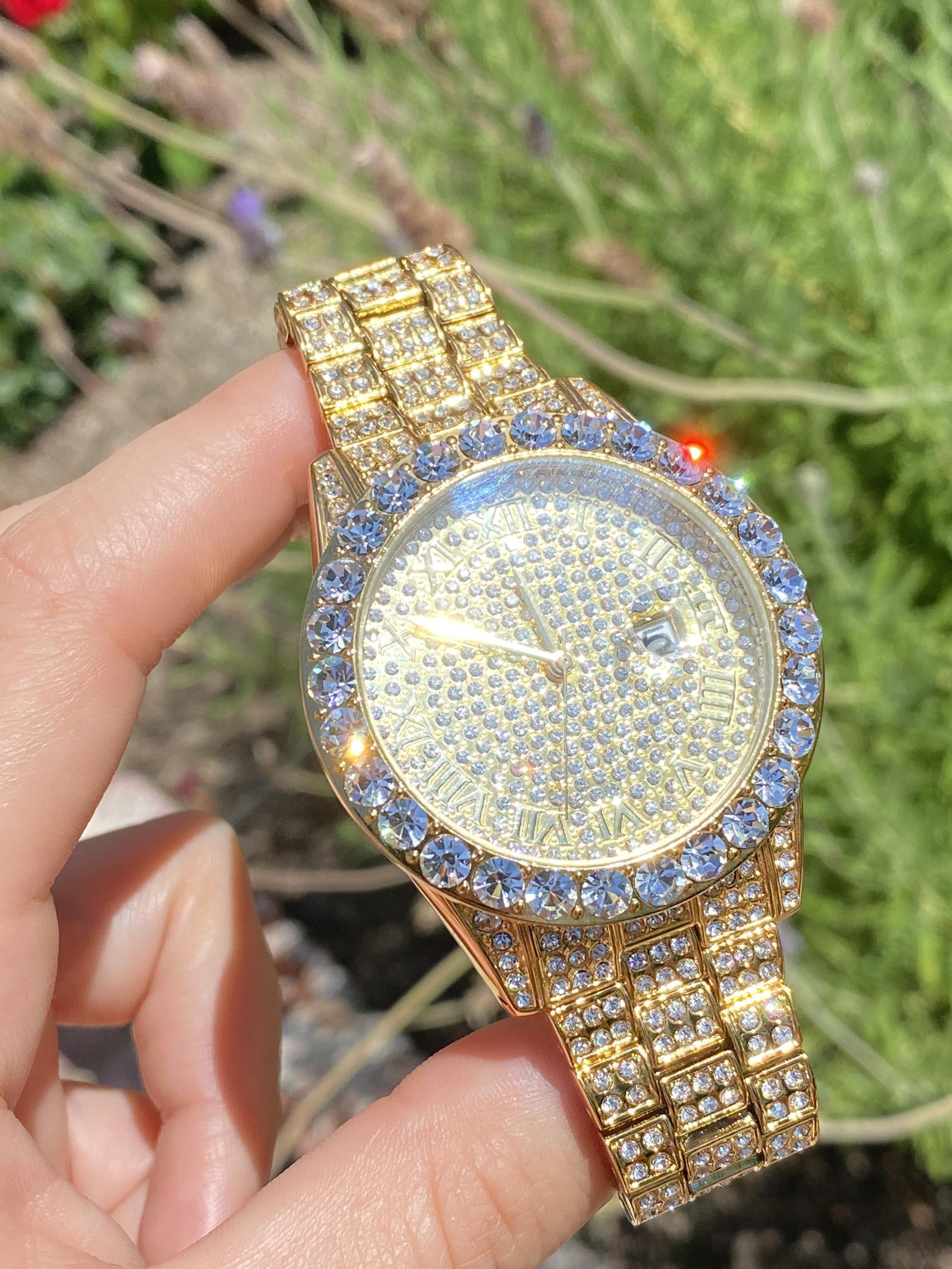 Gold-tone women's and men's watch with a diamond-studded bezel and a sparkling crystal-encrusted band. The watch features a textured gold dial, Roman numeral markers, and a date display at the 3 o'clock position, offering a luxurious and elegant look.