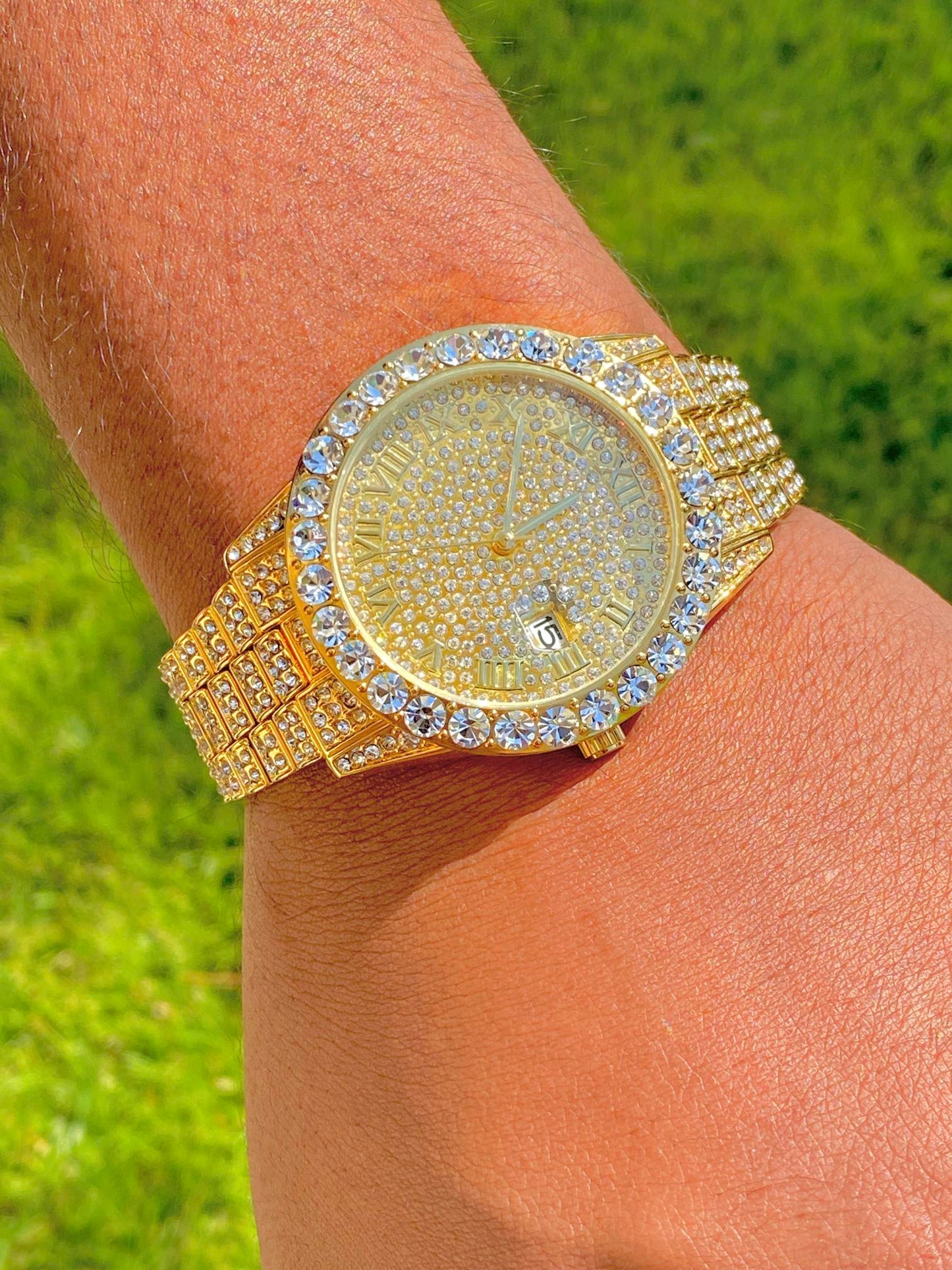 Gold-tone women's and men's watch with a diamond-studded bezel and a sparkling crystal-encrusted band. The watch features a textured gold dial, Roman numeral markers, and a date display at the 3 o'clock position, offering a luxurious and elegant look.