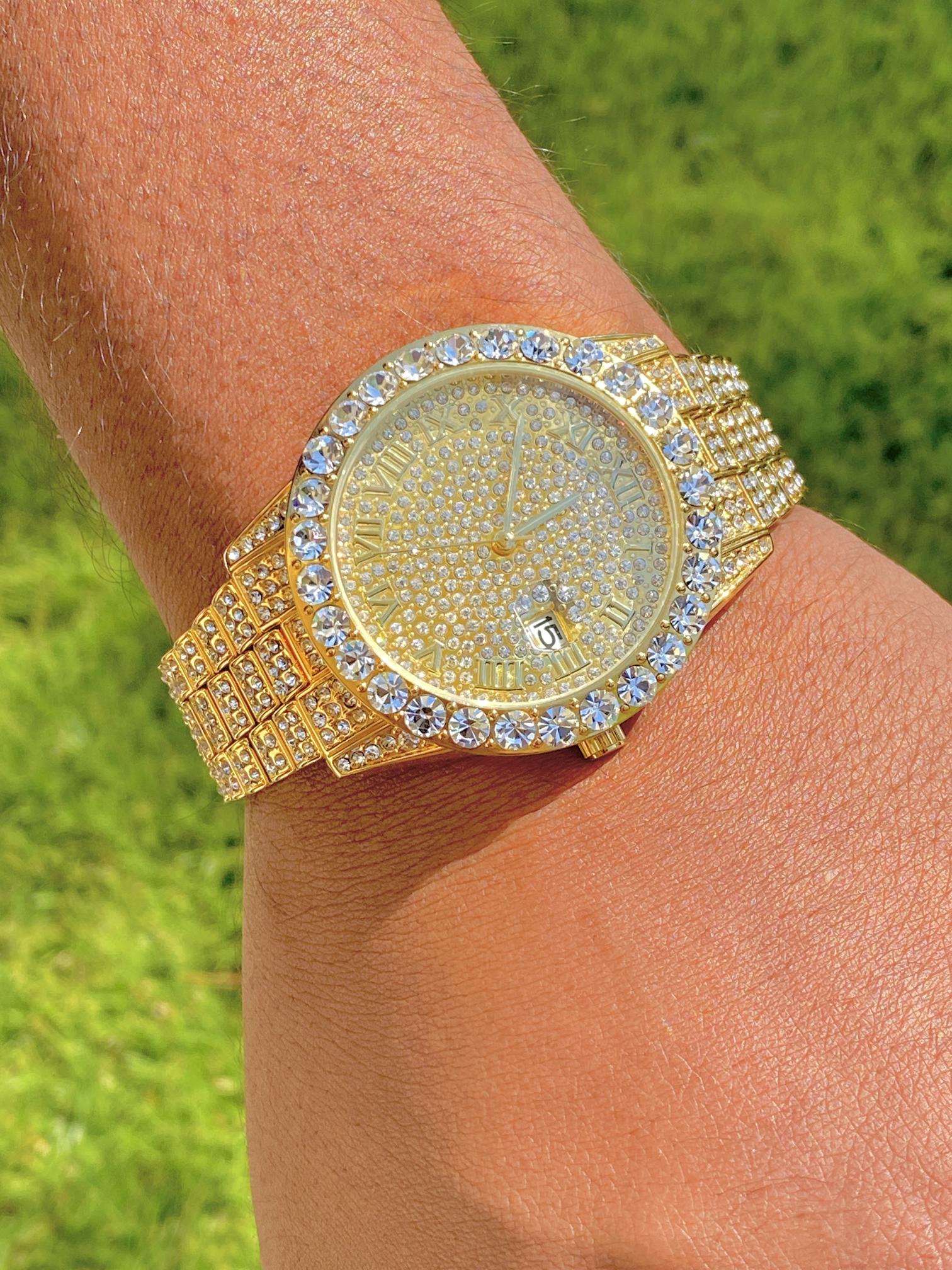 Gold-tone women's and men's watch with a diamond-studded bezel and a sparkling crystal-encrusted band. The watch features a textured gold dial, Roman numeral markers, and a date display at the 3 o'clock position, offering a luxurious and elegant look.