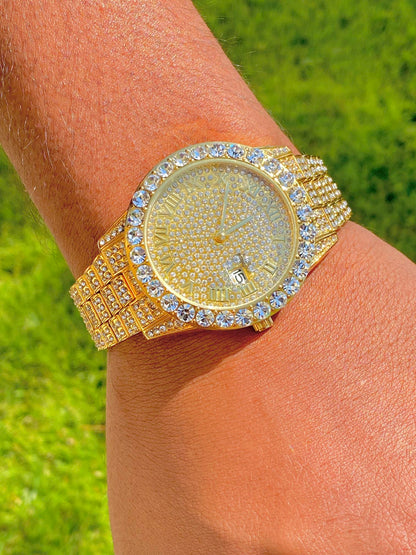 Gold-tone women's and men's watch with a diamond-studded bezel and a sparkling crystal-encrusted band. The watch features a textured gold dial, Roman numeral markers, and a date display at the 3 o'clock position, offering a luxurious and elegant look.